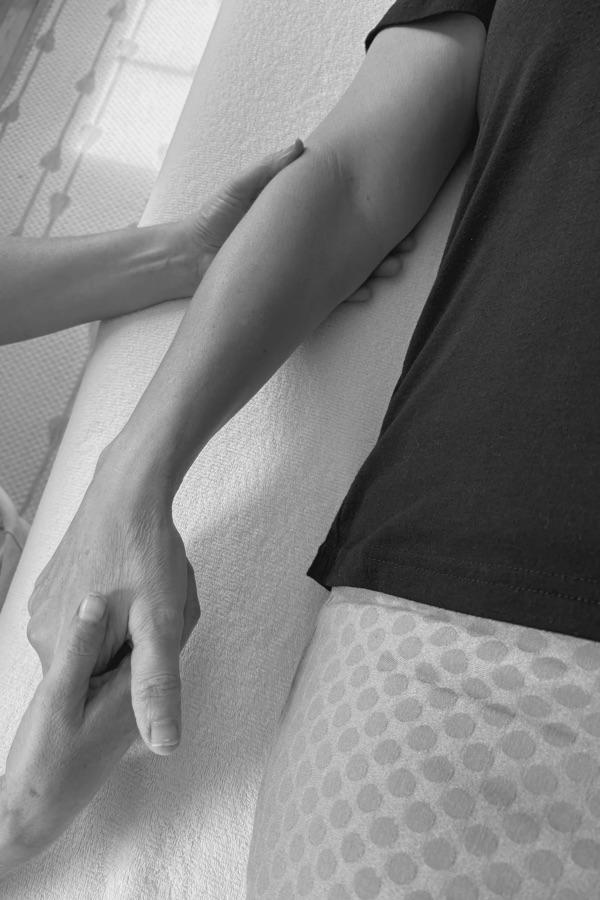 An osteopathic physician's hands gently evaluating a patient's forearm during treatment